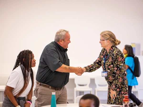 A teacher and a group of young students sit around a classroom table using colourful blocks and shapes to learn numbers and patterns during an interactive maths lesson.

