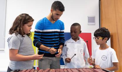 Children water a small plant together outdoors.