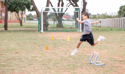  A group of Junior School students dressed in white taekwondo uniforms perform coordinated moves on a green mat during the Annual Sports Day on the school field.