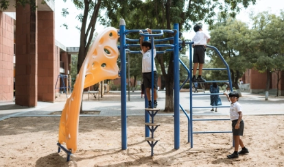  A student smiles while jumping over small yellow hurdles on the school field, with orange cones and buildings in the background.