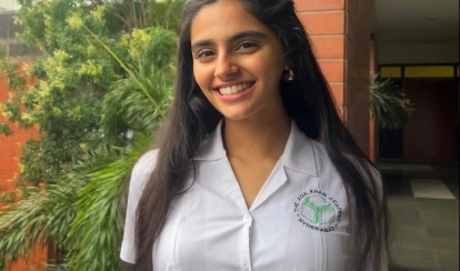 A student from AKA Hyderabad in a white hijab assists two female students in green uniforms at a computer in a classroom setting.