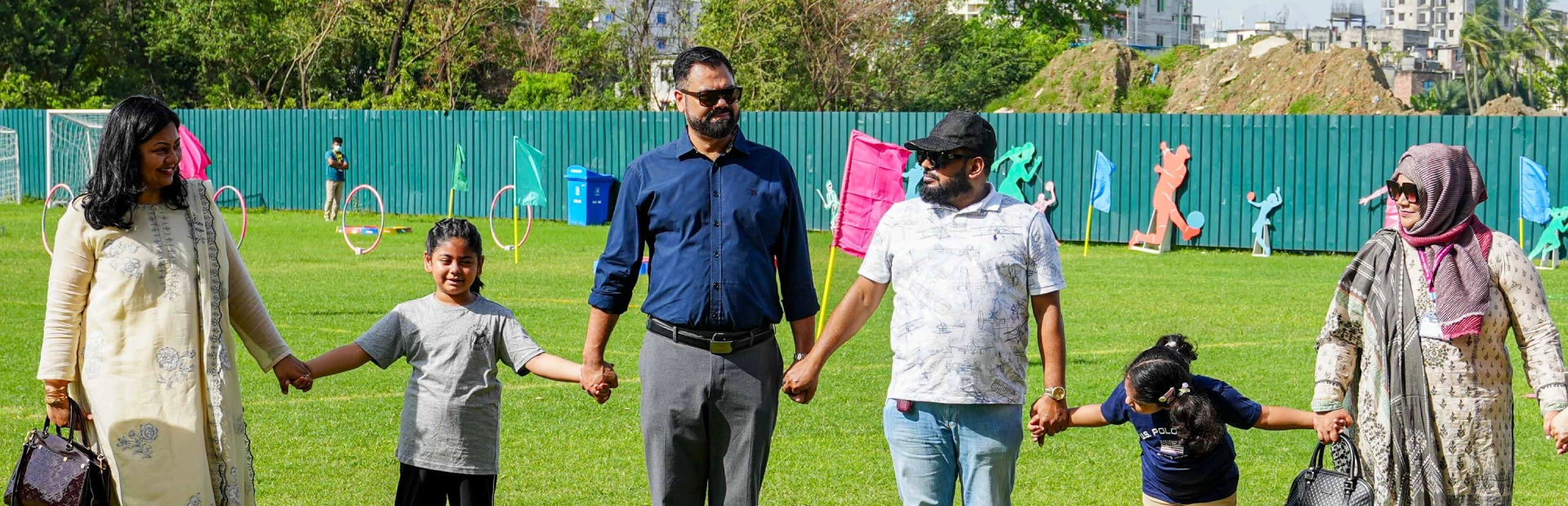 Parents and students hold hands on the school field during the Fun Fit Fest enjoying a sunny day filled with outdoor activities and family fun.