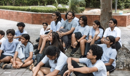 Children water a small plant together outdoors.