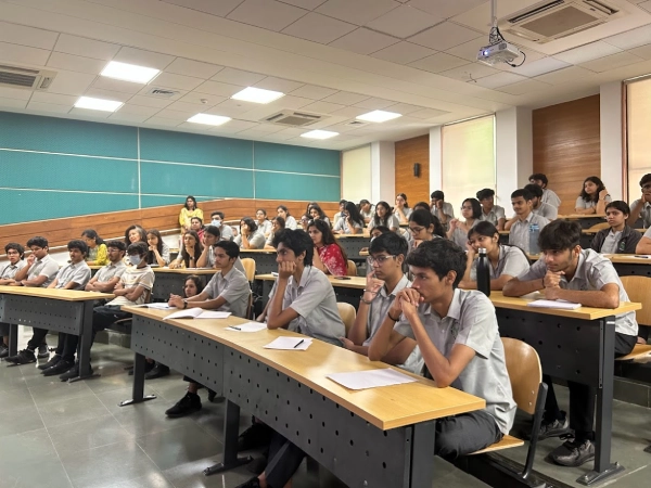 Three DP students sit together discussing their studies while using a laptop and notebooks at a classroom table.