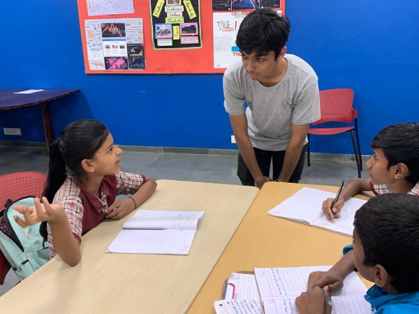 A teacher and a group of young students sit around a classroom table using colourful blocks and shapes to learn numbers and patterns during an interactive maths lesson.

