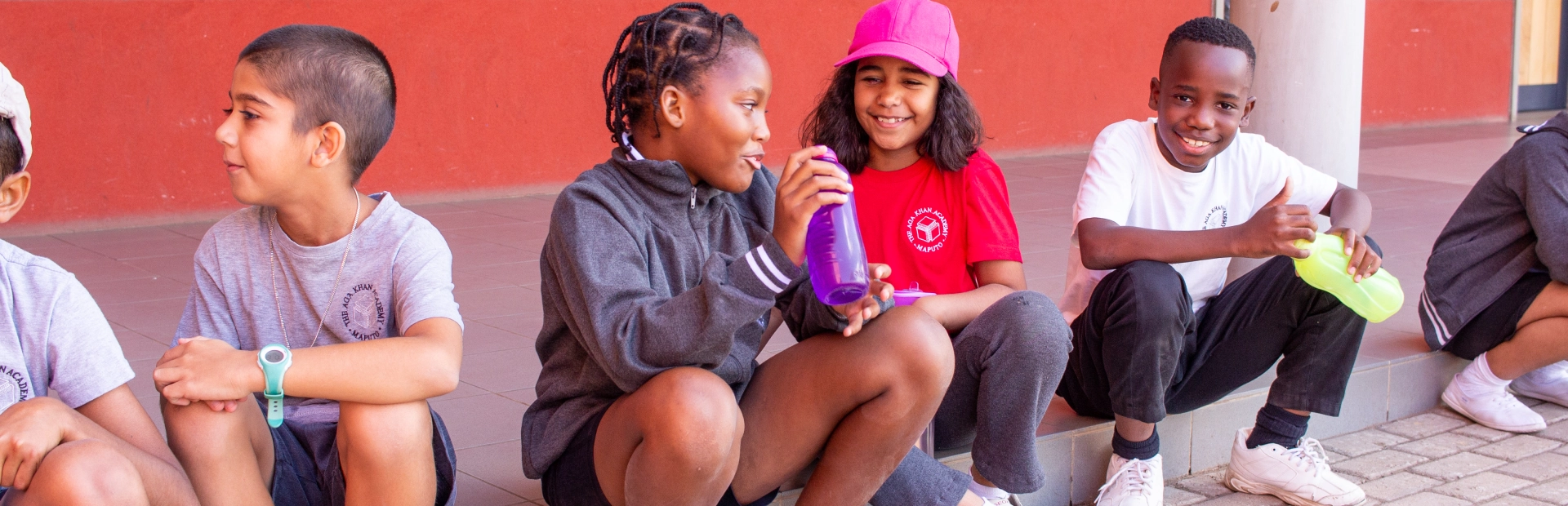 Students sitting on a curb together, with one student looking at the camera and smiling and the others talking to each other.