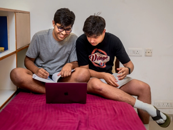 Students studying together on a bed in the dorm room.