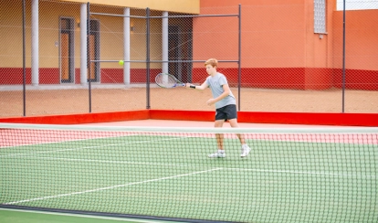 Two students stand together in the library reading a book, surrounded by bookshelves and other students browsing in the background.