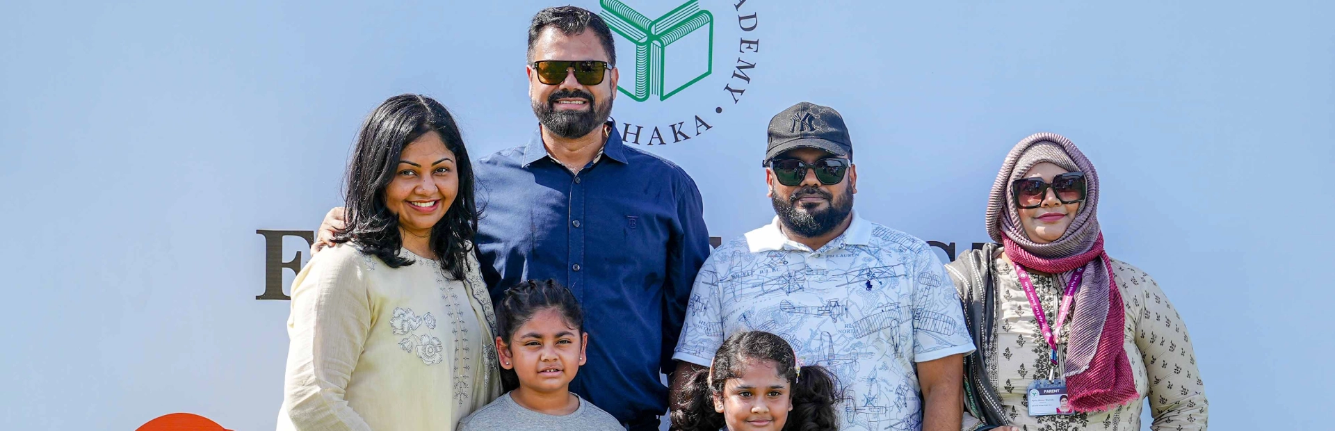 A group of parents and students are smiling and looking at the camera while standing in front of a signage for an event at the Academy