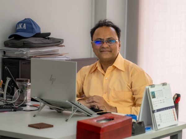 Malik Mahedmood sits at his desk with a laptop, smiling while working in his office