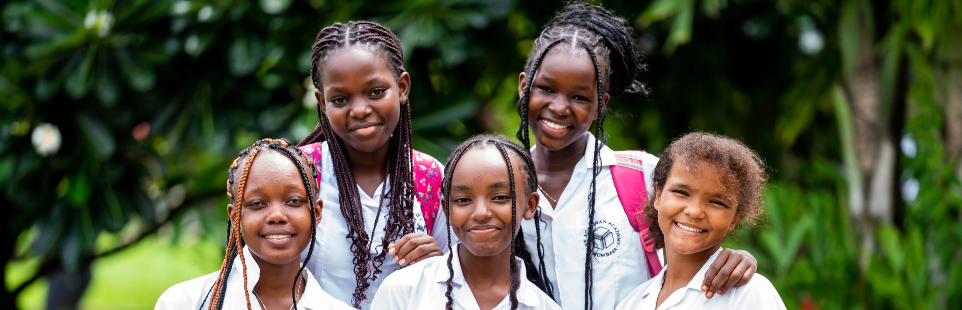 Two young students wearing grey school hoodies sit at a classroom table, smiling and discussing a colourful picture book together.