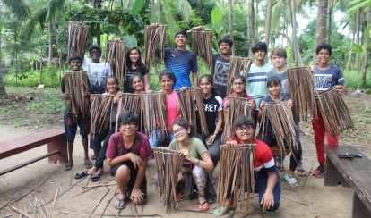  A student smiles while jumping over small yellow hurdles on the school field, with orange cones and buildings in the background.