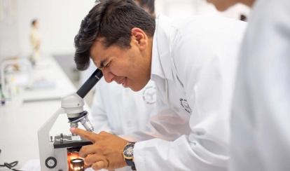  A student smiles while jumping over small yellow hurdles on the school field, with orange cones and buildings in the background.