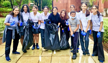 Students at a bake sale stall outdoors on campus; one student serves desserts while others line up to purchase items, surrounded by baked goods, utensils, and cooking supplies, as part of a fundraising event for service learning projects.