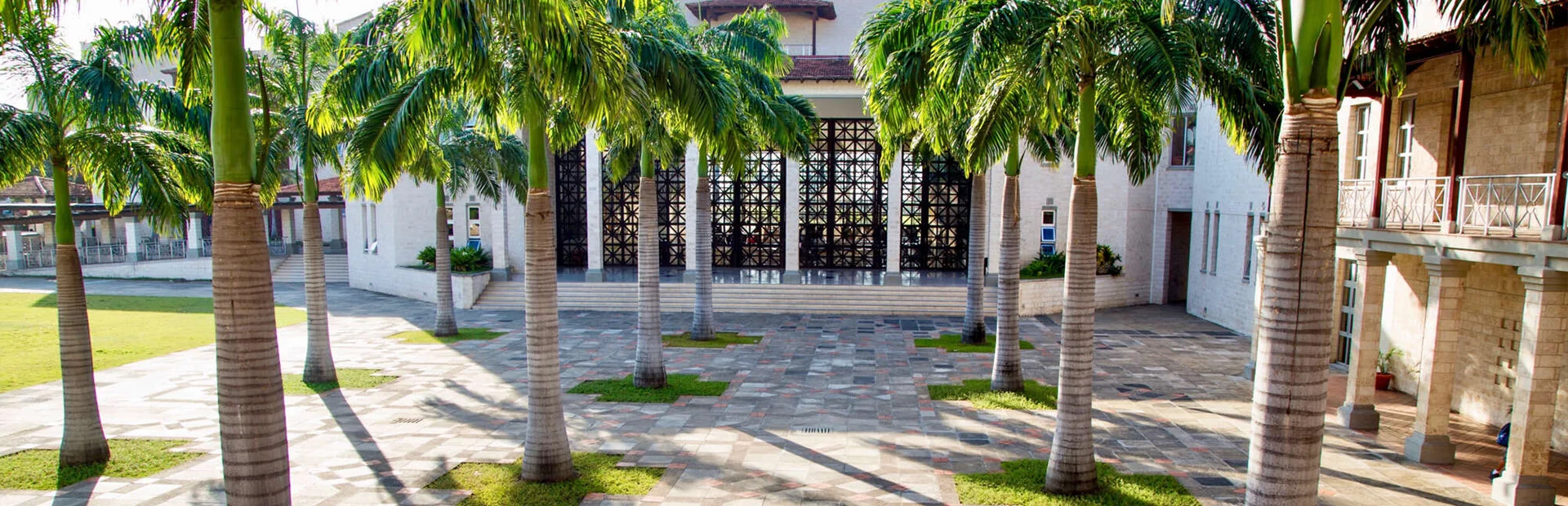 A group of students stand in formation on the school field performing morning exercises in front of the red-brick academic buildings under a clear sky.