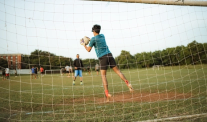  A student smiles while jumping over small yellow hurdles on the school field, with orange cones and buildings in the background.