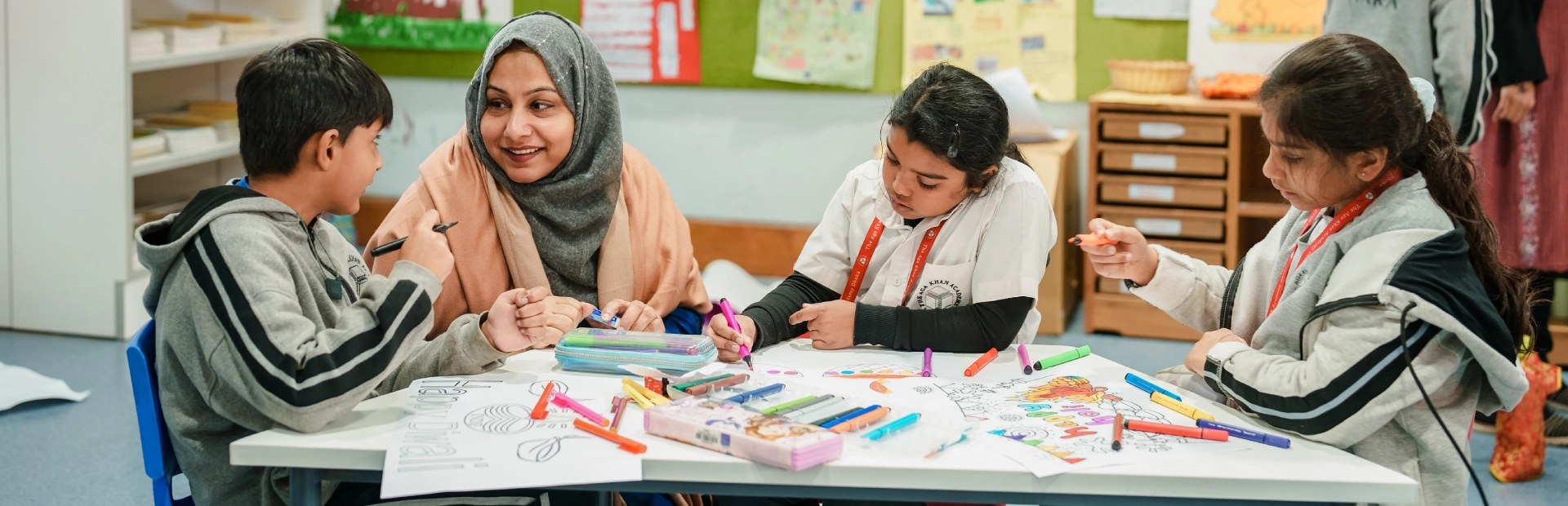 Students and a teacher at AKA Dhaka work together in a classroom on a table.
