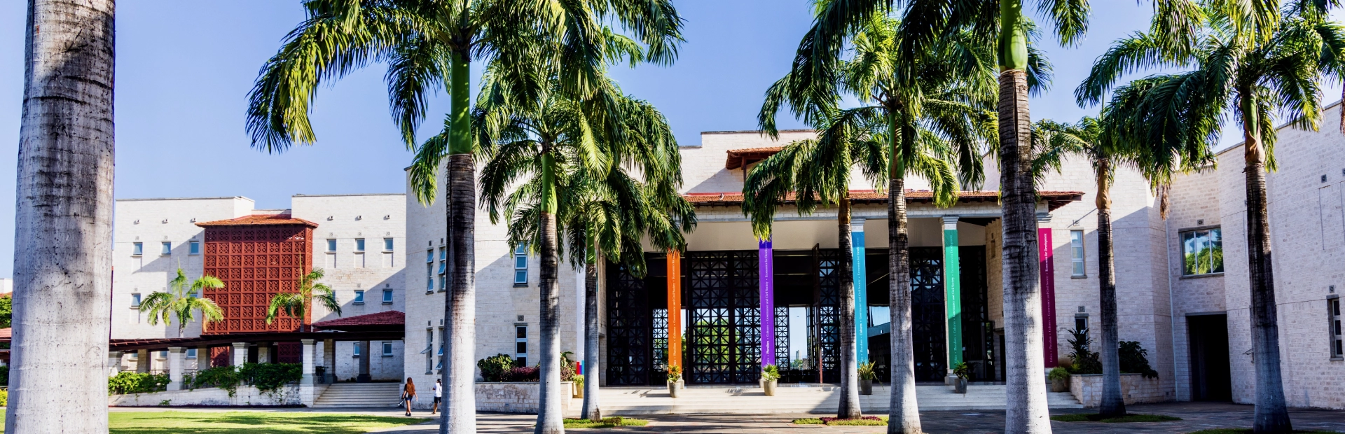 A wide view of the Aga Khan Academy Dhaka campus featuring its red-brick buildings, open green football fields, and clear blue sky.