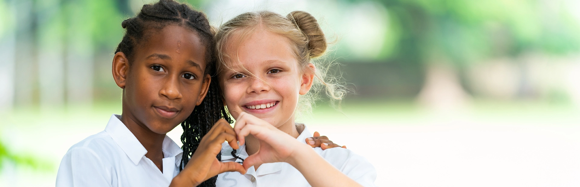 Two students looking at the camera while making hearts with their hands.