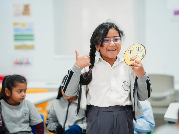 A young student at AKA Dhaka smiles and holds up her artwork during a classroom activity.