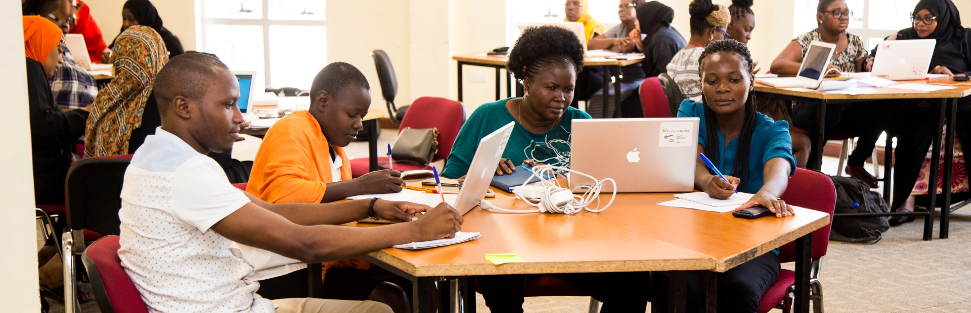  A group of teachers sit on a table, working on their laptops