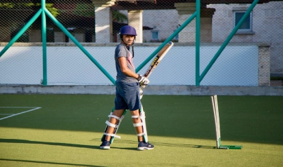 Student playing cricket on astroturf.