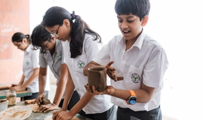 A group of students at AKA Dhaka sit around a table in the art studio, painting vibrant artworks on canvas with brushes and pastels.