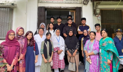 A group of students and staff members of BERNOSSUS pose together for a photo outside the entrance to the community health centre.
